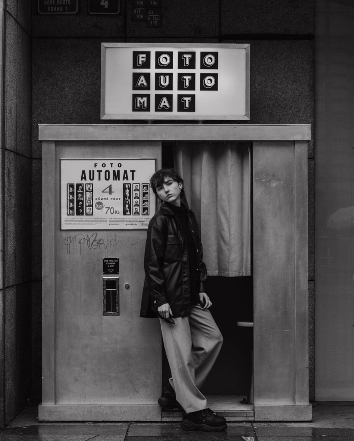 jeune femme en chemise de cuir et pantalon debout devant un photomaton 