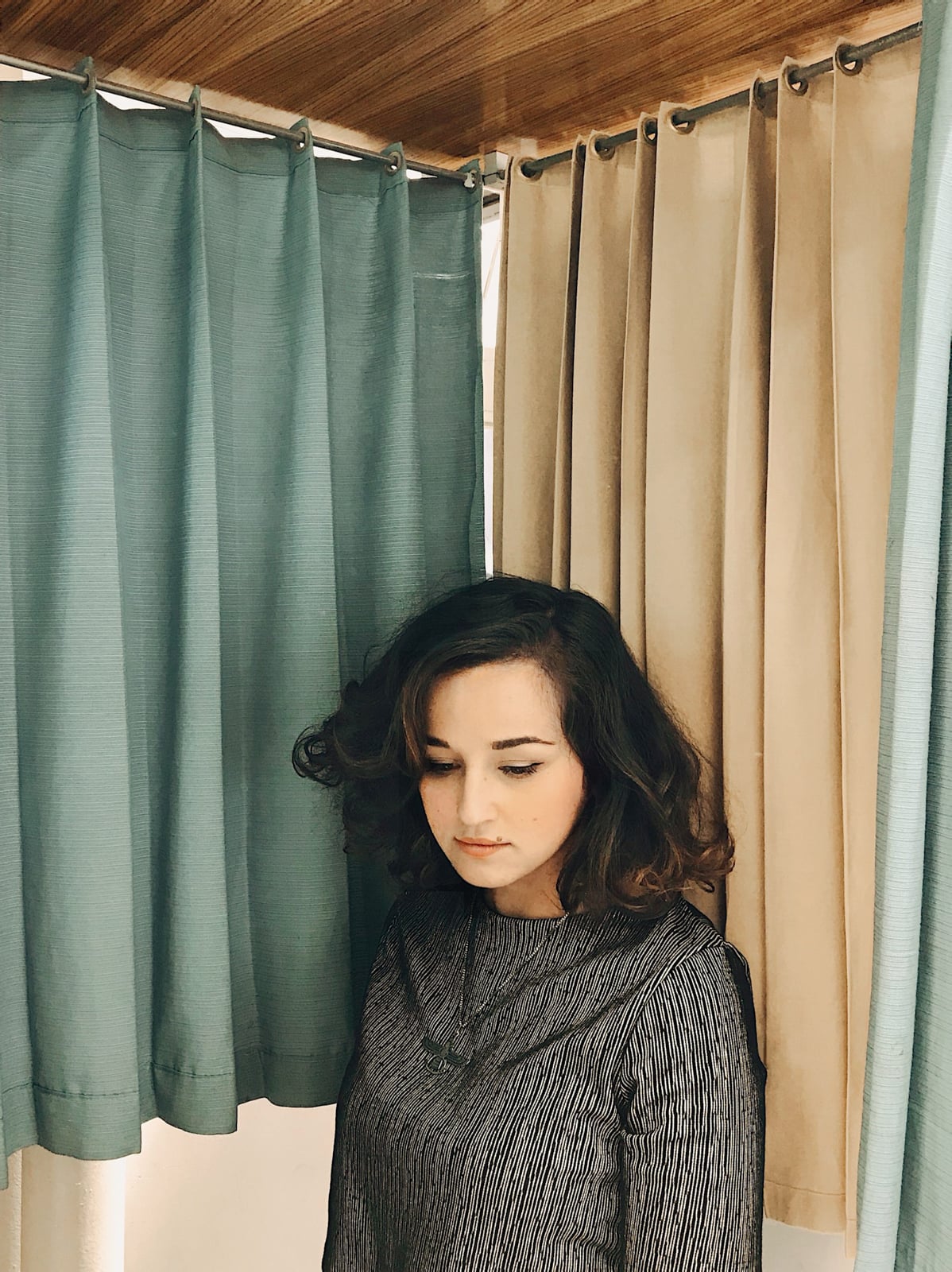 brown woman in gray sweater surrounded by blue and beige curtains of photo booth