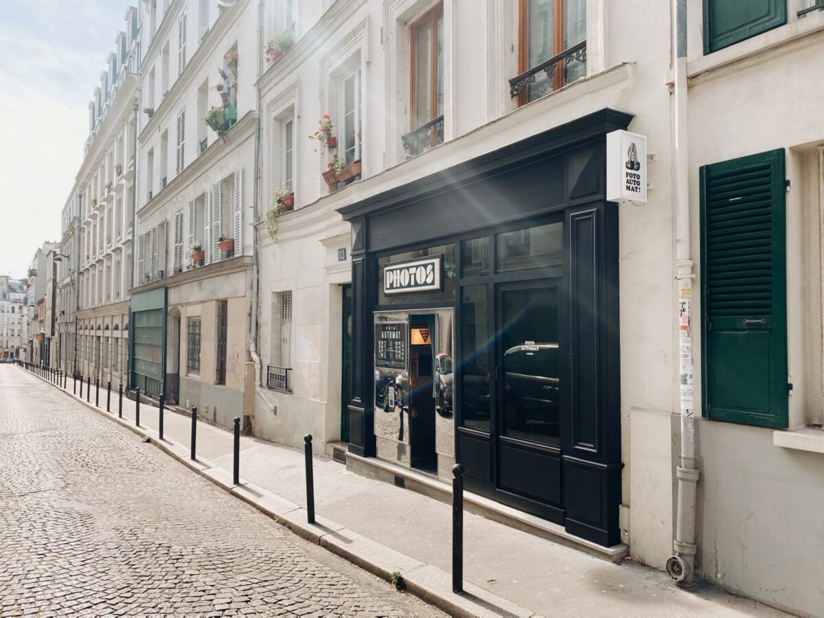 boutique avec une devanture noire et un photomaton en façade dans une rue ensoleillée 